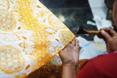 Surakarta, Endonezya 7 Ağustos 2020: Kumaşın altın batik arka planıyla Canting. Batik Tulis çizimi