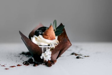 Beyaz krema çiçeğiyle süslenmiş, çikolata parçalı kurabiyeler ve bir yaprak parçasıyla tamamlanmış el yapımı pasta. Ve büyük bir yaban mersini. Kahverengi el işi kağıdıyla süslenmiş. Kahve çekirdeğinin etrafında.