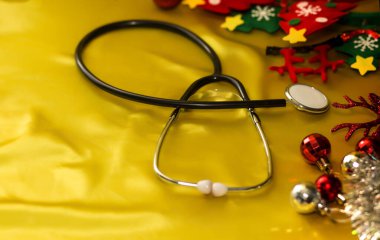 Yeni yıl ve tıp. Noel ağacı için dekoratif oyuncaklarla süslenmiş altın arka planda bir stetoskop. Geçmişi. Hekimler. Sağlık hizmetleri.
