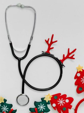 Stetoskop kırmızı Noel boynuzlarıyla süslenmiş. Doktorları tebrik etmek için arka plan. Noel ağaçlarıyla neşeli kafa halkaları.