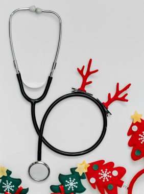The steitoscope is decorated with red Christmas horns. Background for congratulations to doctors. Cheerful head hoops with Christmas trees. clipart