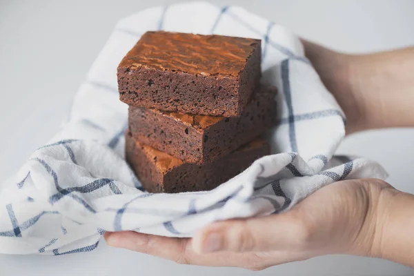 Manos de mujer sosteniendo una alfombra de chocolate brownie con ropa en whit Imagen de archivo