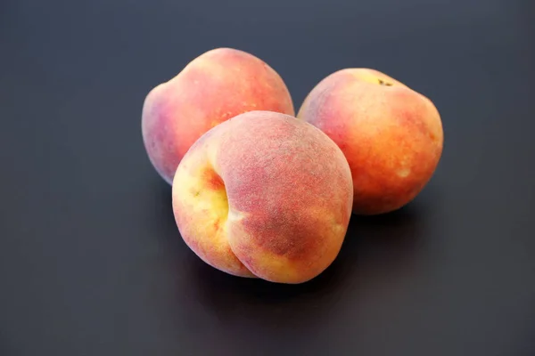 Three juicy ripe peaches on dark gray background cluse up view