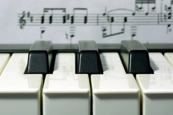 Three black keys of music keyboard with music notes on background macro view, selective focus — Stock Photo, Image