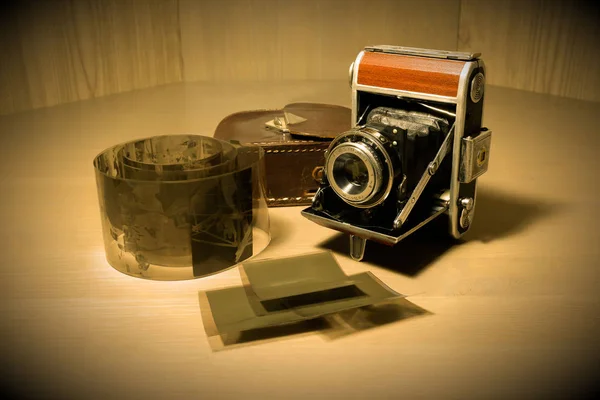 Retro old vintage outdated manual film camera circa 1940s, negative films and leather camera case on wooden table. — Stock Photo, Image