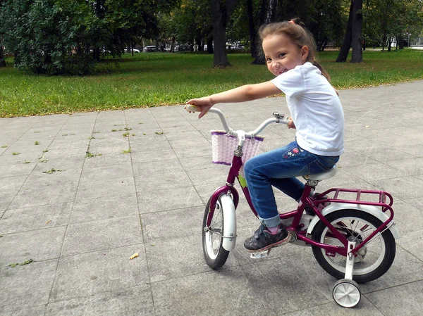 Hermosa niña sonriente montando bicicleta en un camino en un parque —  Fotos de Stock