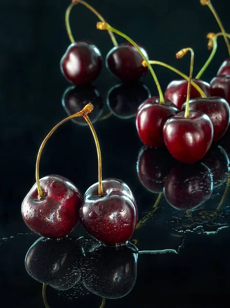 Large sweet cherry reflected on a dark mirror surface