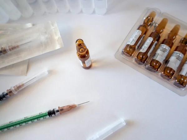 An ampoule of medicine is prepared for injection. On a clean white surface are syringes and ampoules in a package. Medical background for business, pharmacies, clinics, hospitals, treatment rooms.