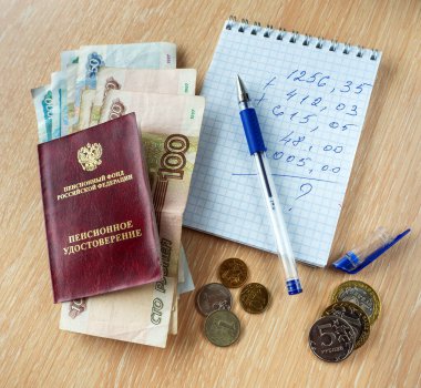 Ruble banknotlar Rusya Federasyonu 'nun emeklilik sertifikası altında. Masanın üzerinde hesaplamalar, kalem ve bozuk paralarla dolu bir defter var..