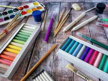 Background with materials for drawing. Pastels in a box, watercolors, brushes and other creative tools are placed on a wooden surface. clipart