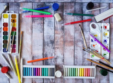 Kutular dolusu pastel boya, suluboya, fırça, keçeli kalemler ve diğer çizim aletleriyle arka plan. Metin için temiz alan.