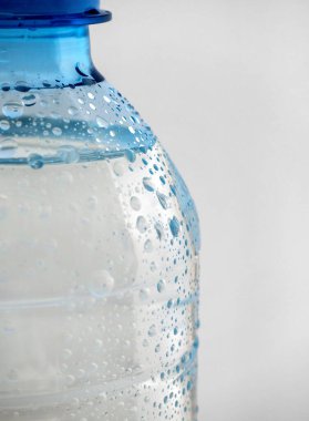 Temiz suyu olan plastik bir şişenin bir parçası beyaz arka planda görülebilir. Şişenin yüzeyinden su damlaları görülebilir..