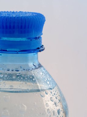 Plastik temiz su şişesinin üstü beyaz arka planda görülebilir. Şişe su damlalarıyla kaplı..