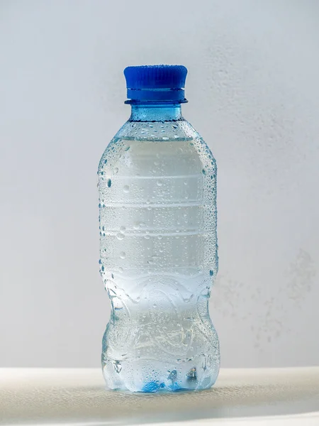 Plastic bottle with clean cold water on a light background. The bottle is closed with a lid. Water drops are visible on the bottle.
