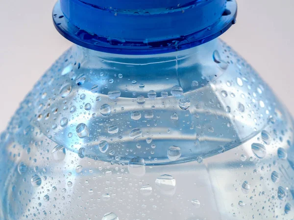 Drops on the surface of a bottle of clean water close-up. Only the top of the bottle is visible.