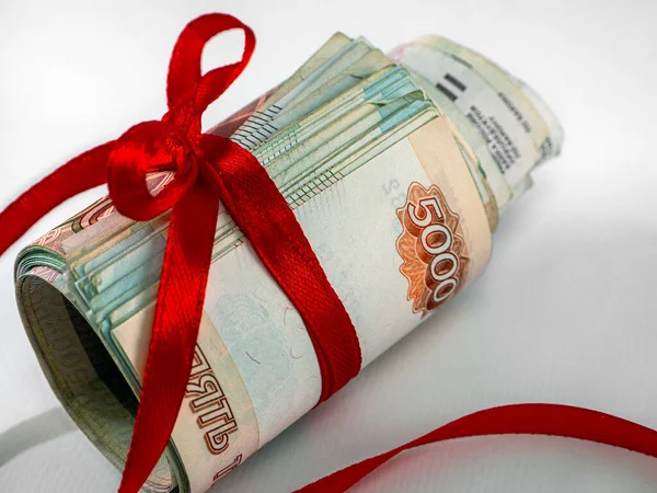 Rus ruble banknotları sarılıp kırmızı kurdeleyle bağlanır ve bir ışık yüzeyine çapraz olarak dizilir. Yakın plan. Rus Rublesi ile mali arkaplan.