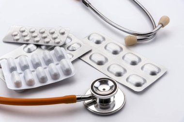 Kapsüllerde ilaç kabarcıkları terapi için haplar ve beyaz arka planda steteskop.
