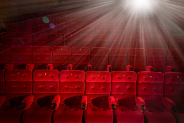 Kırmızı koltukları ve parlak projektör ışığı olan sinema salonu.