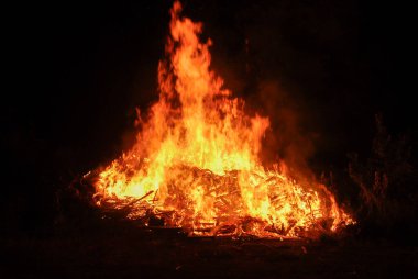 Ateş gece dışarıda yanar, büyük yanan odun ateşi hareket halindeki alevler siyaha bulanır.