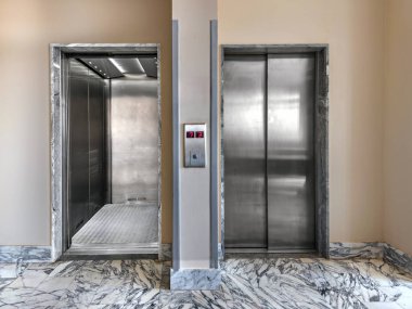 İki sedye asansörü, biri paslanmaz çelik kapılı asansör ve diğeri de hastanede beyaz mermer döşemeli yerde açık ve boş..
