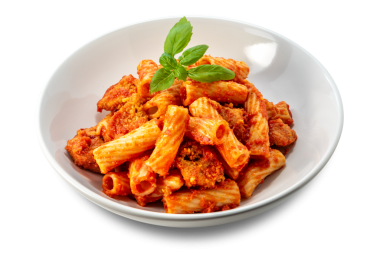 Domates soslu makarna, et parçaları ve beyaz tabakta taze fesleğen yaprakları.