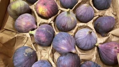 Siyah görev incirleri karton sandıkta dizilmiş. Mor incirlerin üstündeki görüntüyü takip ediyorlar.