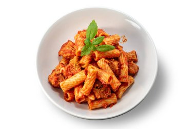 Domates soslu makarna, köfte parçaları ve beyaz tabaktaki taze fesleğen yaprakları.