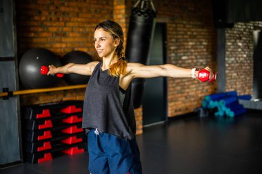 Genç kız spor yapıyor ve spor salonunda farklı egzersizler yapıyor. Spor sağlık demektir. Arka planda birçok spor malzemesi var. Sağlıklı bir yaşam tarzı teması..