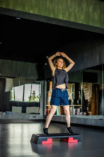 Young girl is doing fitness and different exercises in the gym.Sport is health. Many sports equipment on  e background.Themes of a healthy lifestyle.