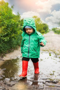 Yavrum. Yeşil ceketli ve kırmızı çizmeli küçük bir çocuk bataklıkta oynuyor. Tasasız bir çocukluk. Mutlu çocuk konsepti. Mutlu bir çocukluk geçiriyor. Çığlık atıyor, gülüyor, bataklıkta eğleniyor..