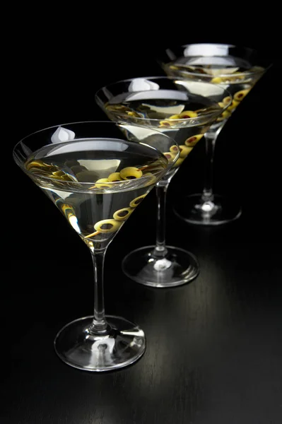 Three Martini drinks with olives isolated on black table — Stock Photo, Image