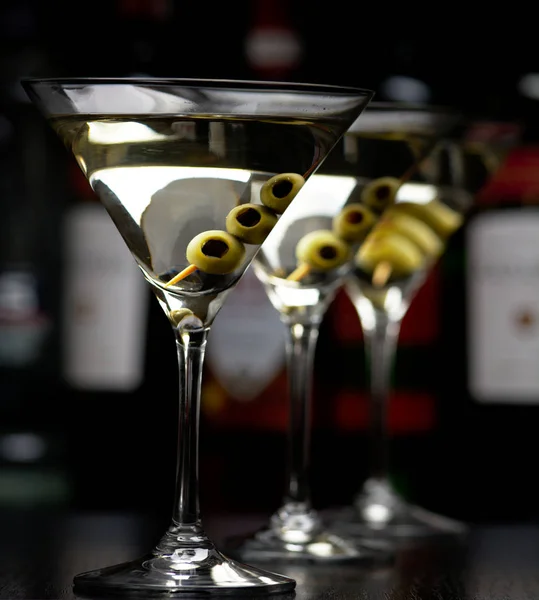 Три коктейля мартини с оливками на палочке в клубе на черном столе — стоковое фото