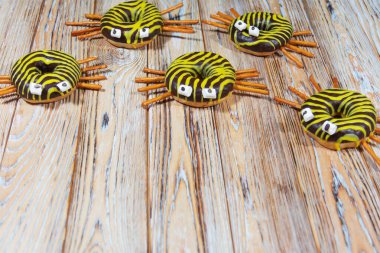 Ahşap yüzeyde beş örümcek şekilli çörek, çizgili krema, şeker gözlü ve kraker bacaklı. Şenlikli Cadılar Bayramı ziyafeti, eğlenceli tasarım, üst görünüm, kırsal arka plan.