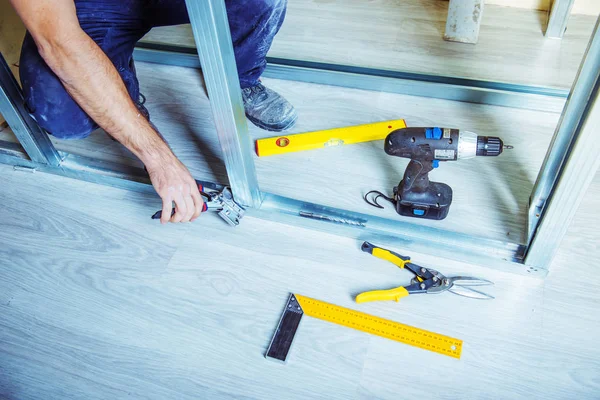 Alçıpan alçı çıpanı iş başında. Tadilat sırasında bir evde metal alçıpan inşa ederken elinde çivi çakma aleti tutan ve kullanan bir kişi