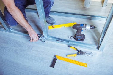 Alçıpan alçı çıpanı iş başında. Tadilat sırasında bir evde metal alçıpan inşa ederken elinde çivi çakma aleti tutan ve kullanan bir kişi