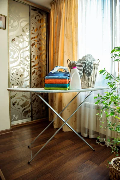 Electric iron and basket of clean linen on ironing board, against the window