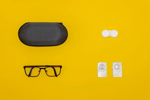Glasses, contact lenses and storage cases on yellow background