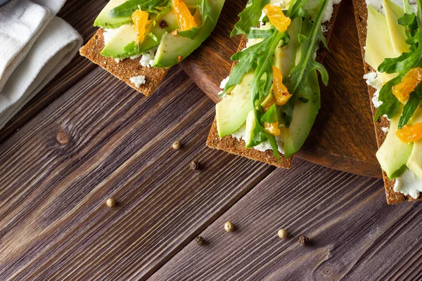 Pão crocante integral com queijo, folhas de foguete e tangerina em pano de fundo de madeira — Fotografia de Stock
