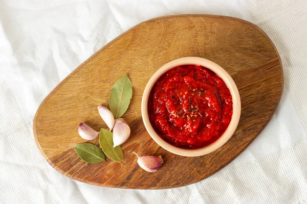 Ajvar in a bowl, garlic and spicy leaves on a wooden board. Serbian traditional food. — Stock Photo, Image