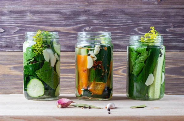 Homemade pickled vegetables in a jars: cucumbers, paprica and garlic with herbs on a wooden background. The canned or fermented vegetarian food concept.