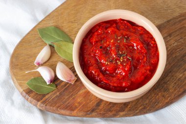 Ajvar, tahtanın üzerinde sarımsak ve baharatlı yapraklarla dolu bir kasede. Sırp veya Balkan geleneksel yemekleri.