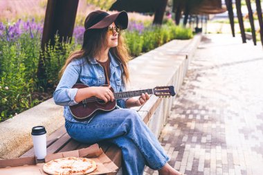 Modern parkta ukulele çalan şapkalı güzel bir kadın..