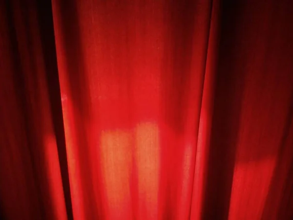 Primer plano de las cortinas de color rojo oscuro en una habitación. Tejido - terciopelo denso, con la luz del día entrando en la parte posterior de la cual la iluminación es visible en la tela —  Fotos de Stock