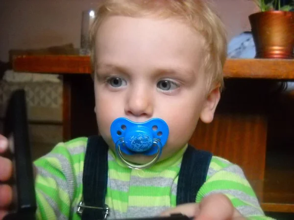 A criança está interessada no assunto na mesa. A boca do bebê tem um mamilo azul . — Fotografia de Stock