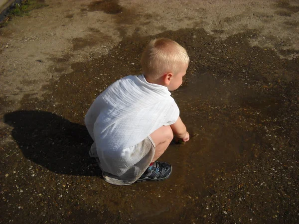 Un niño pequeño juega en una piscina en mal estado cuando hace calor. El niño tiene zapatos mojados —  Fotos de Stock