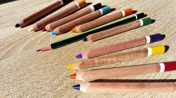 Holzstifte in verschiedenen Farben liegen auf einem beigen Tisch. Darunter sticht ein längerer Graphitstift hervor. Unähnlichkeit, Unterschied — Stockfoto