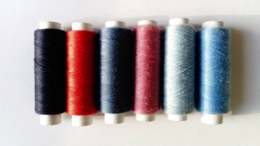 Babunlar ve farklı renklerde iplik makaraları. Close. Bir tarafta doğal ışık var. Beyaz arka plan. Mavi, kırmızı, pembe, gri ve siyah