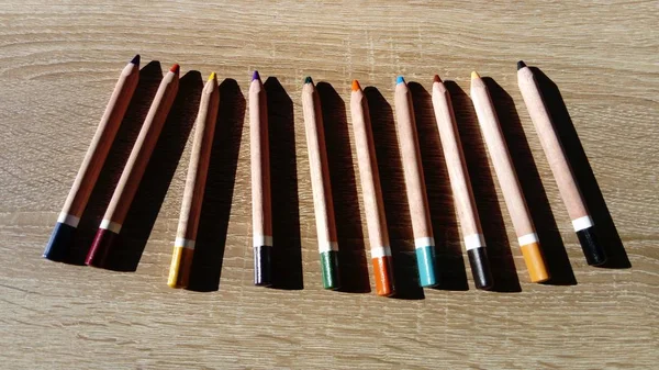 On a wooden table are wooden thick colored pencils. Hard light — Stock Photo, Image