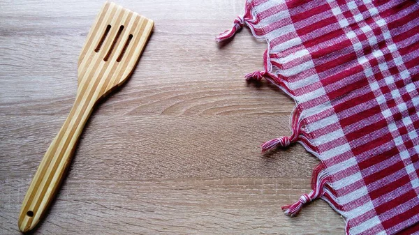 A wooden spatula for stirring cooked food. A kitchen tablecloth made of red-and-white checked fabric is on the right — Stock Photo, Image