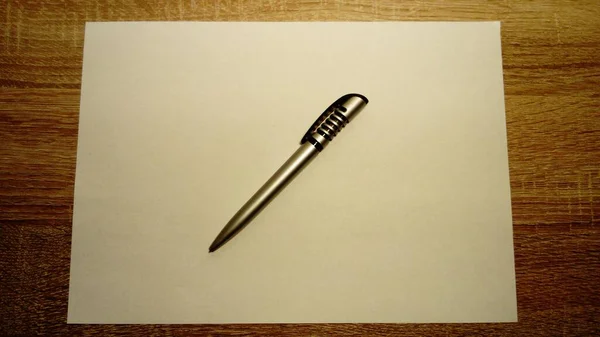 Een balpen ligt op een wit vel papier. Papier en pen liggen op een houten tafel — Stockfoto